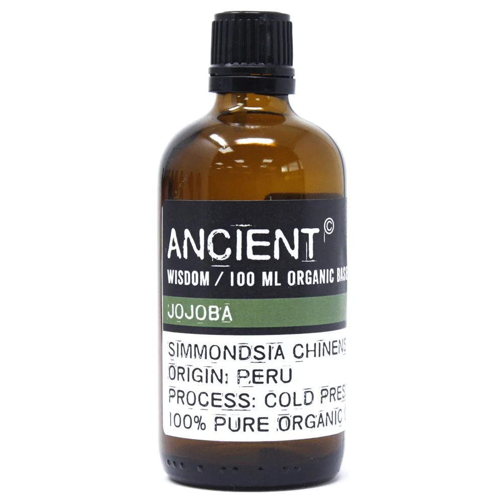 Transparent glass bottle holding dark amber liquid, label reads Jojoba Organic Base Oil indicating organic jojoba oil.