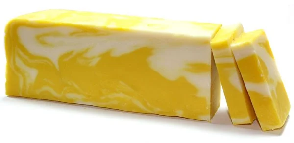 Lemon olive oil soap loaf on natural wood surface, sliced to reveal bright citrus foam.