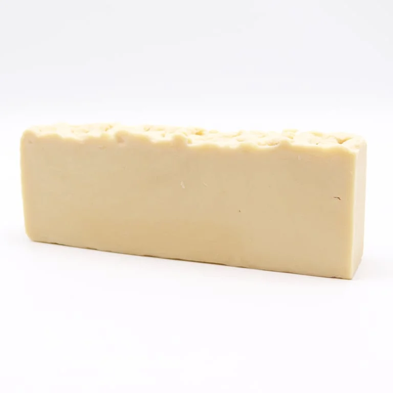 donkey milk olive oil soap loaf sitting on a wooden cutting board with a splash of olive oil beside it