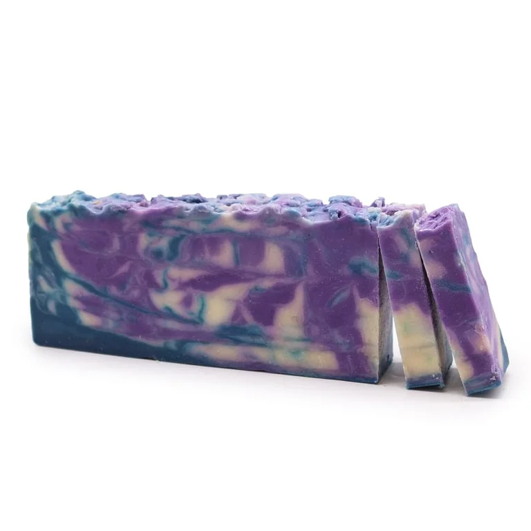 A rectangular loaf of olive oil soap with greenish hue and subtle herb trimming, displayed on a natural wooden surface.