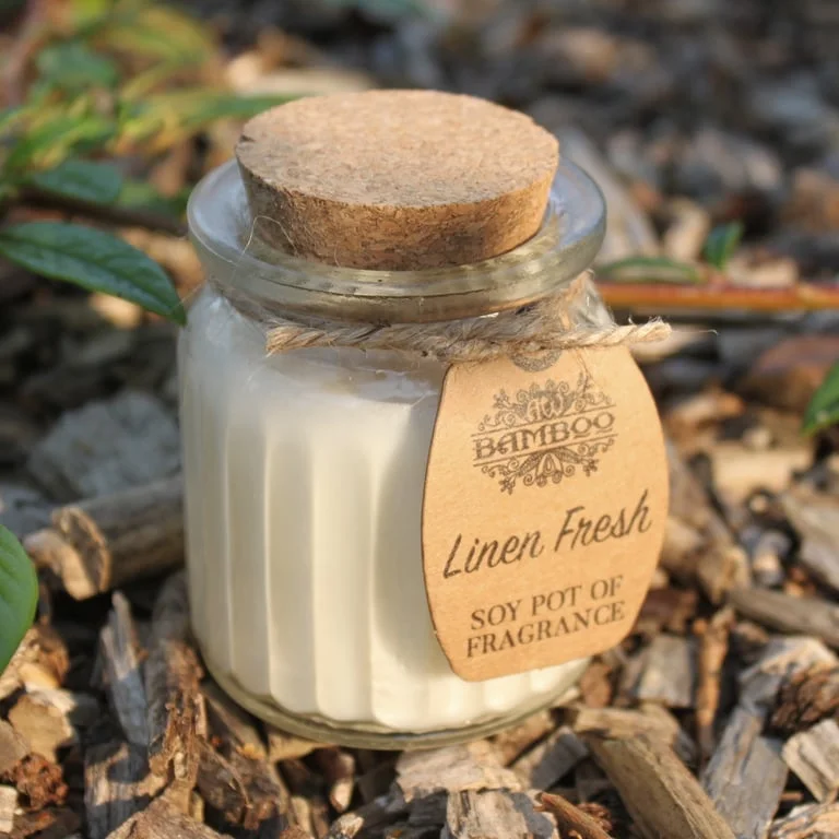 Fresh linen soy candle displayed in a clear ceramic pot, showing wax and a white wick.