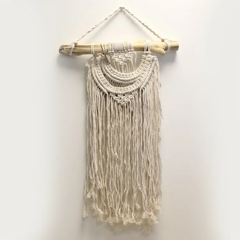Macrame wall hanging with two wave patterns in intricate knotting, hanging on a gable wall.