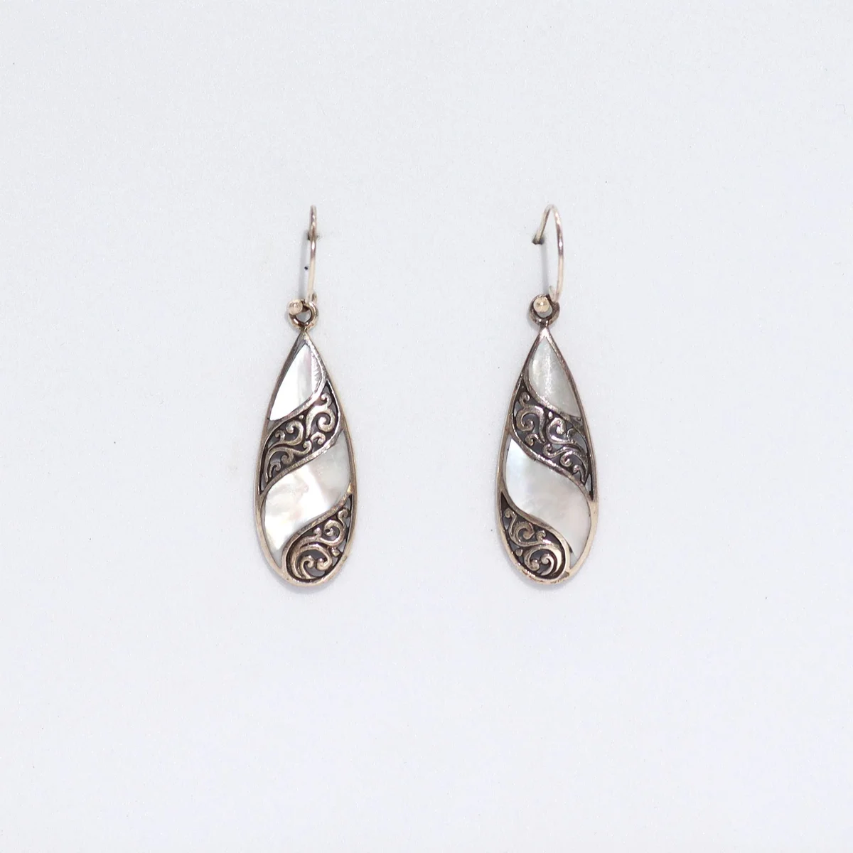 Silver shell teardrop earrings floating against plain background.