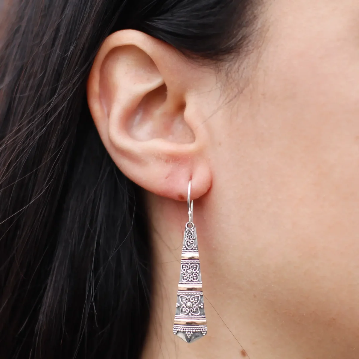 Silver earrings in tribal drop style accented by gold details displayed on a neutral background.