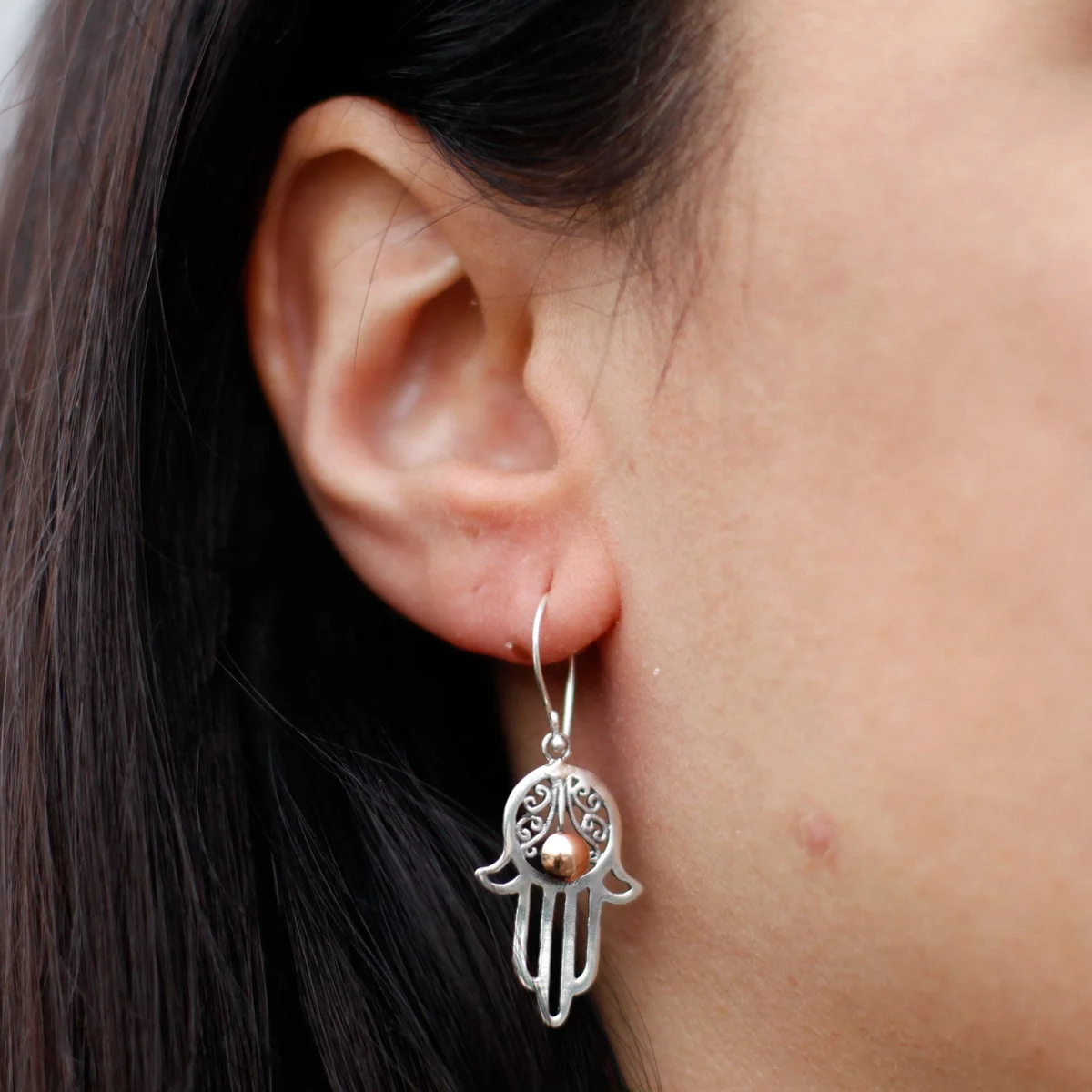 Silver and gold hamsa earrings: ornate hand symbols hanging from delicate chains.