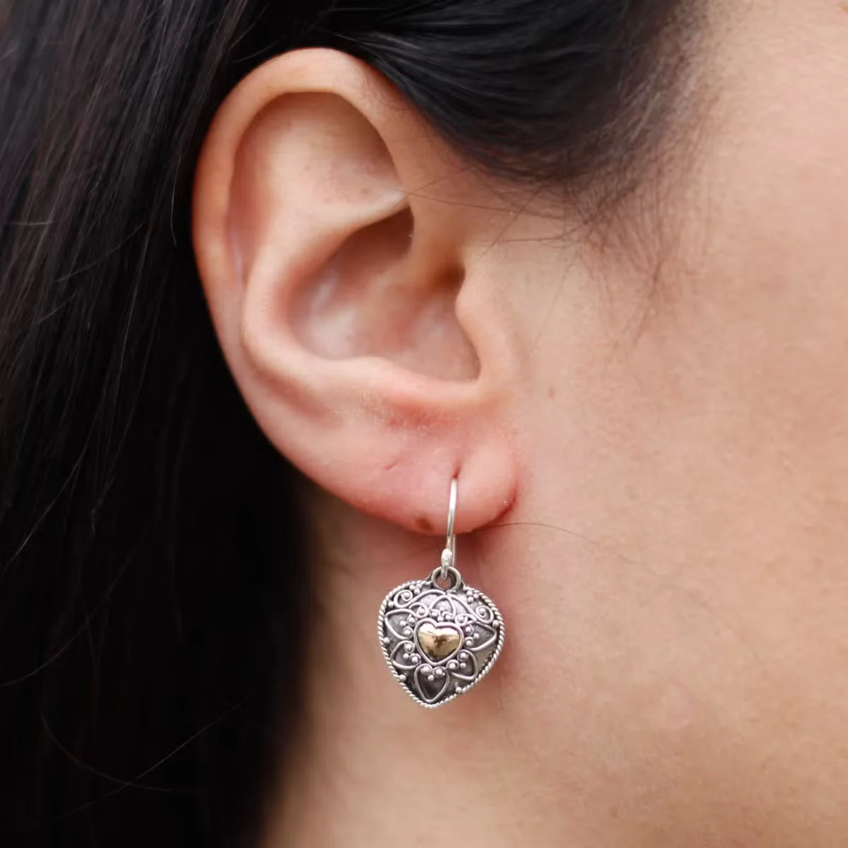 Pair of stylish silver earrings featuring mandala heart design with silver and gold tones on white background