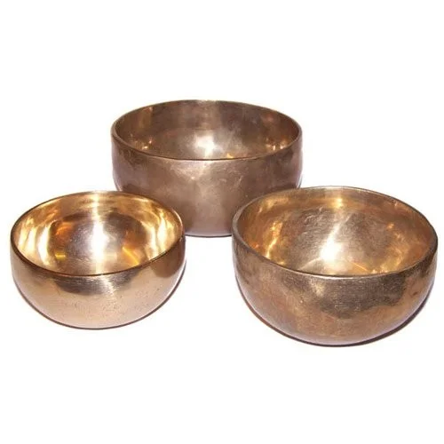 Set of three handmade brass singing bowls displayed on a wooden surface
