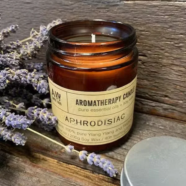 Aromatherapy scented candle labeled "Aphrodisiac" on a small white holder.