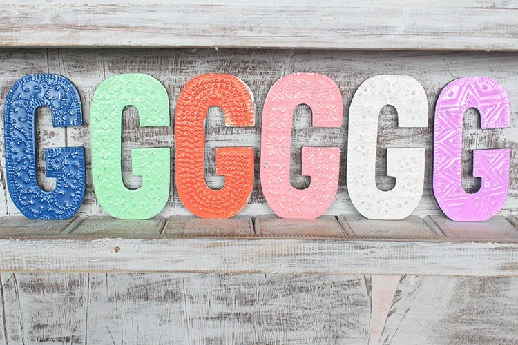 Letter G wall decor, assorted colours, 15cm tall, seen hanging on a wall.
