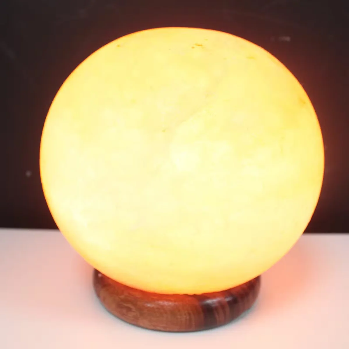 Round natural salt lamp ball on a large wooden base, glowing softly against a plain background