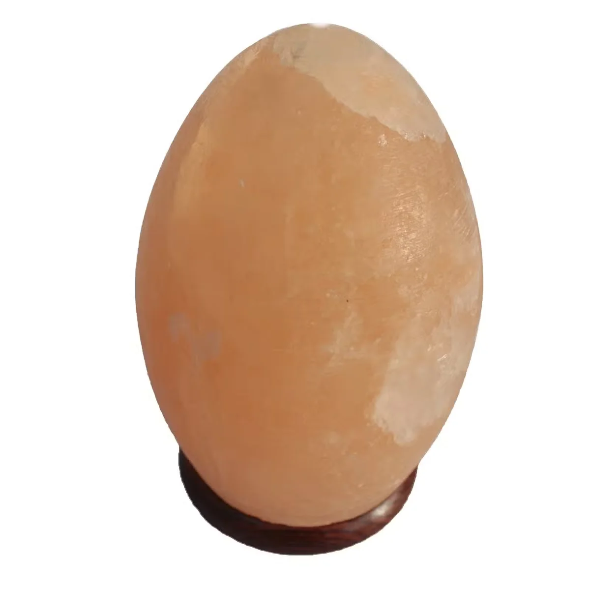 Egg shaped lamp made from salt with a smooth wooden base, softly glowing against a plain background