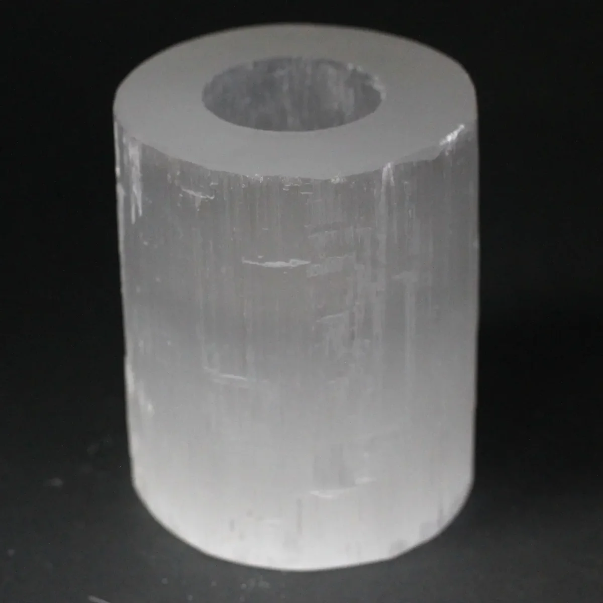 Selenite cylindrical candle holder, 10 cm tall, translucent crystal with a lit candle inside.