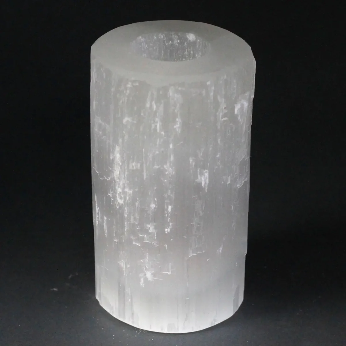 Selenite cylinder candle holder, 15 cm tall, clear glass cylinder holding a lit candle.