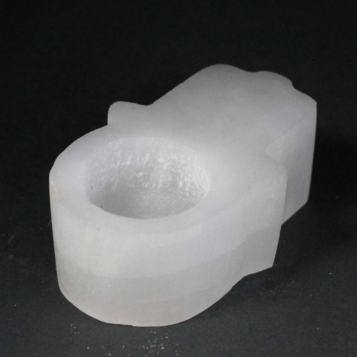 A white translucent selenite candle holder shaped like a hamsa hand, with a small candle inside.
