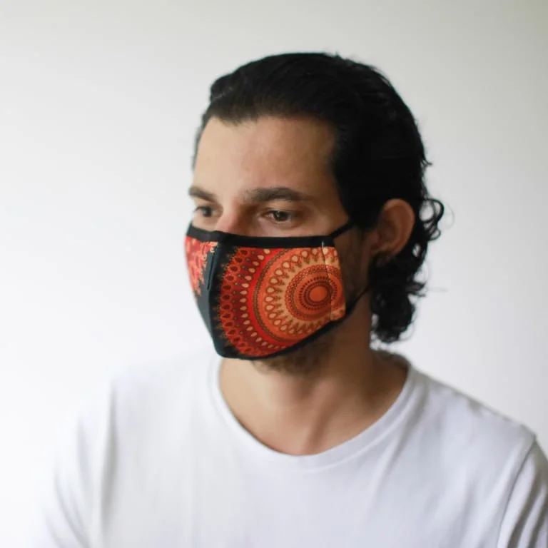 Reusable fashion face mask in bright orange mandala pattern, fitting adult size.