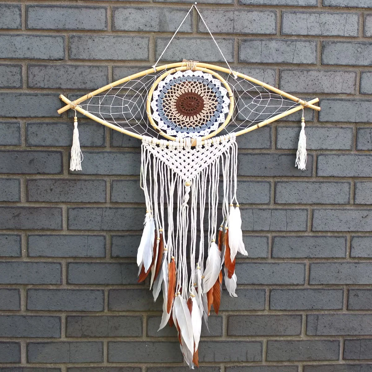 Large macrame white grey brown dream catcher with evil eye design hanging against plain background