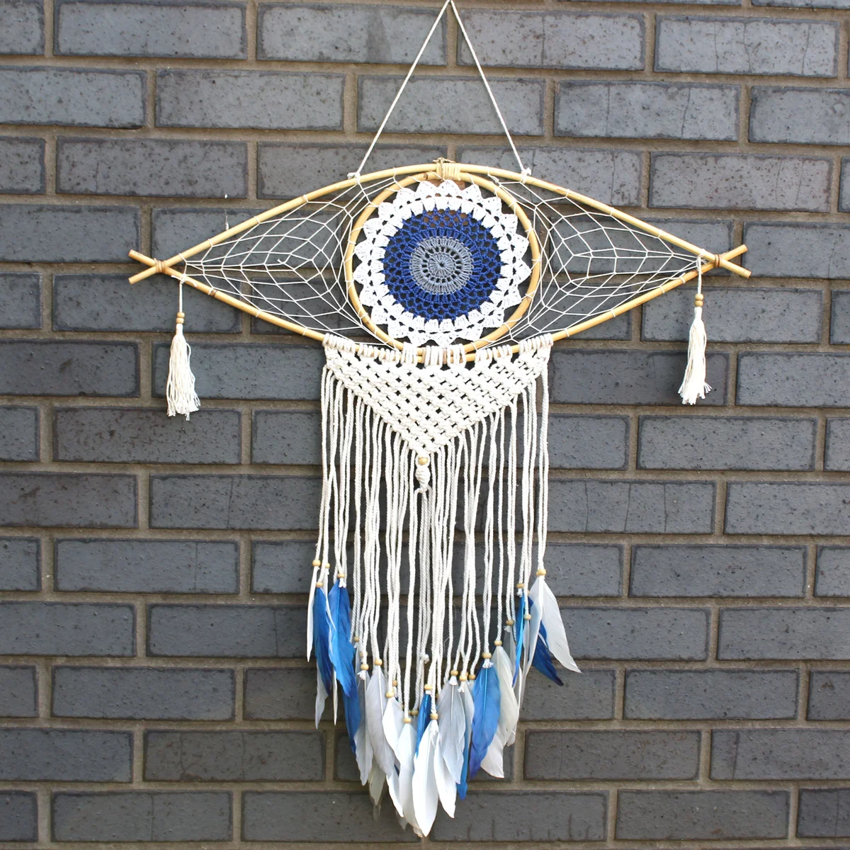 Large macrame dream catcher in white, blue, and grey with evil eye wall decor detail hanging on wall