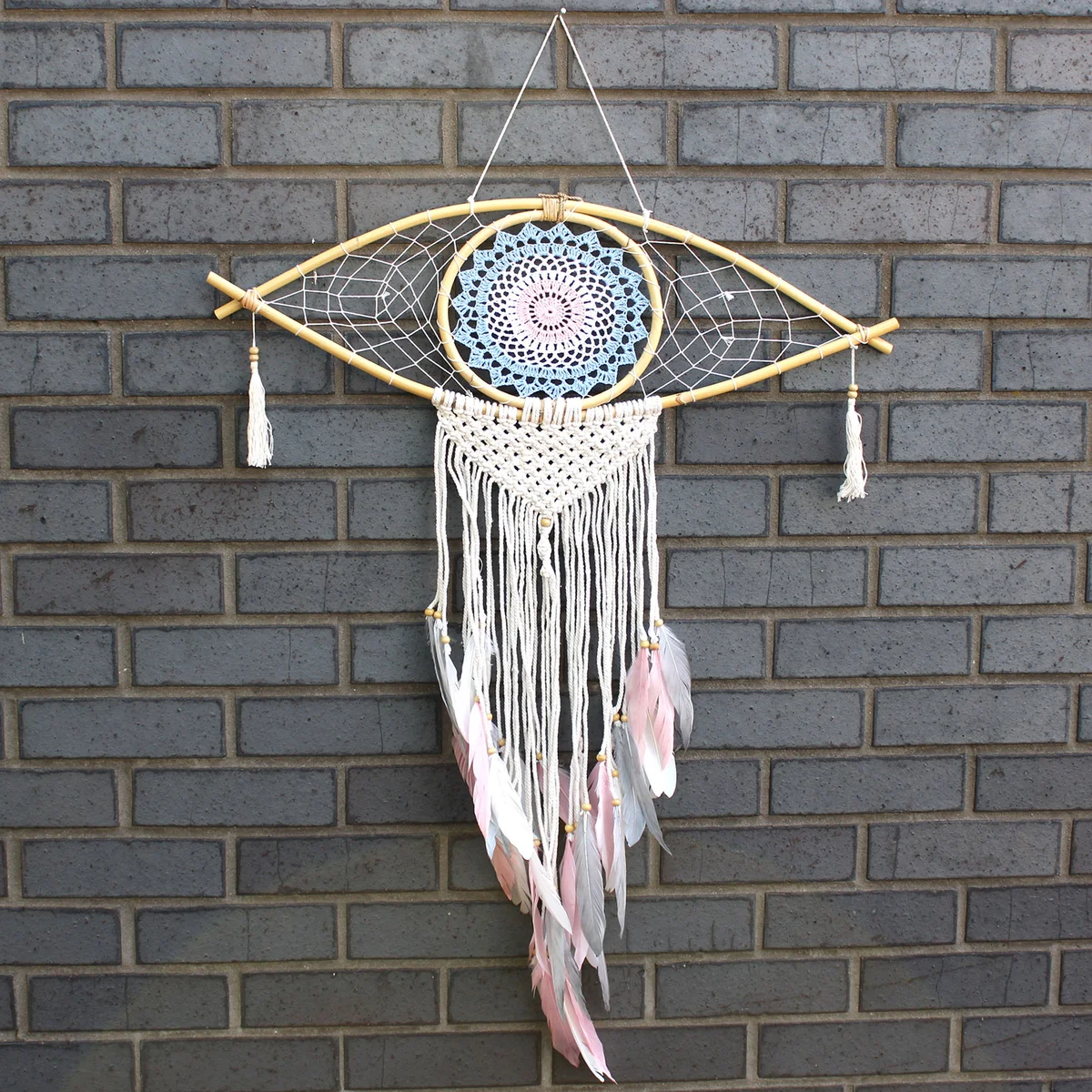 Large macrame blue white pink dream catcher featuring an eye design with hanging tassels and feathers