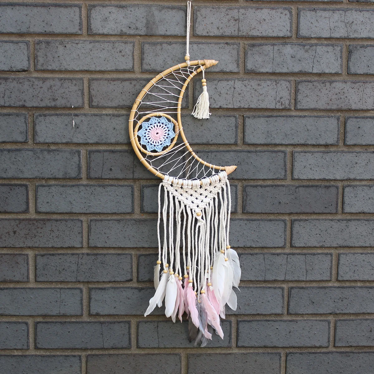 Moon-shaped macrame dream catcher with woven threads and hanging fringe.