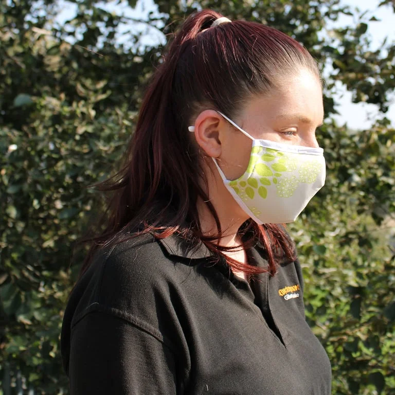 Reusable adult face mask with green leaf pattern, soft fabric and adjustable ties, shown folded for storage.