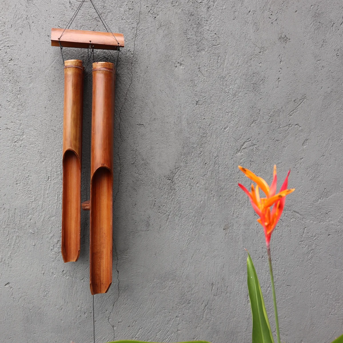 Bamboo windchime with four large tubes in a natural finish hanging outdoors against a blurred background