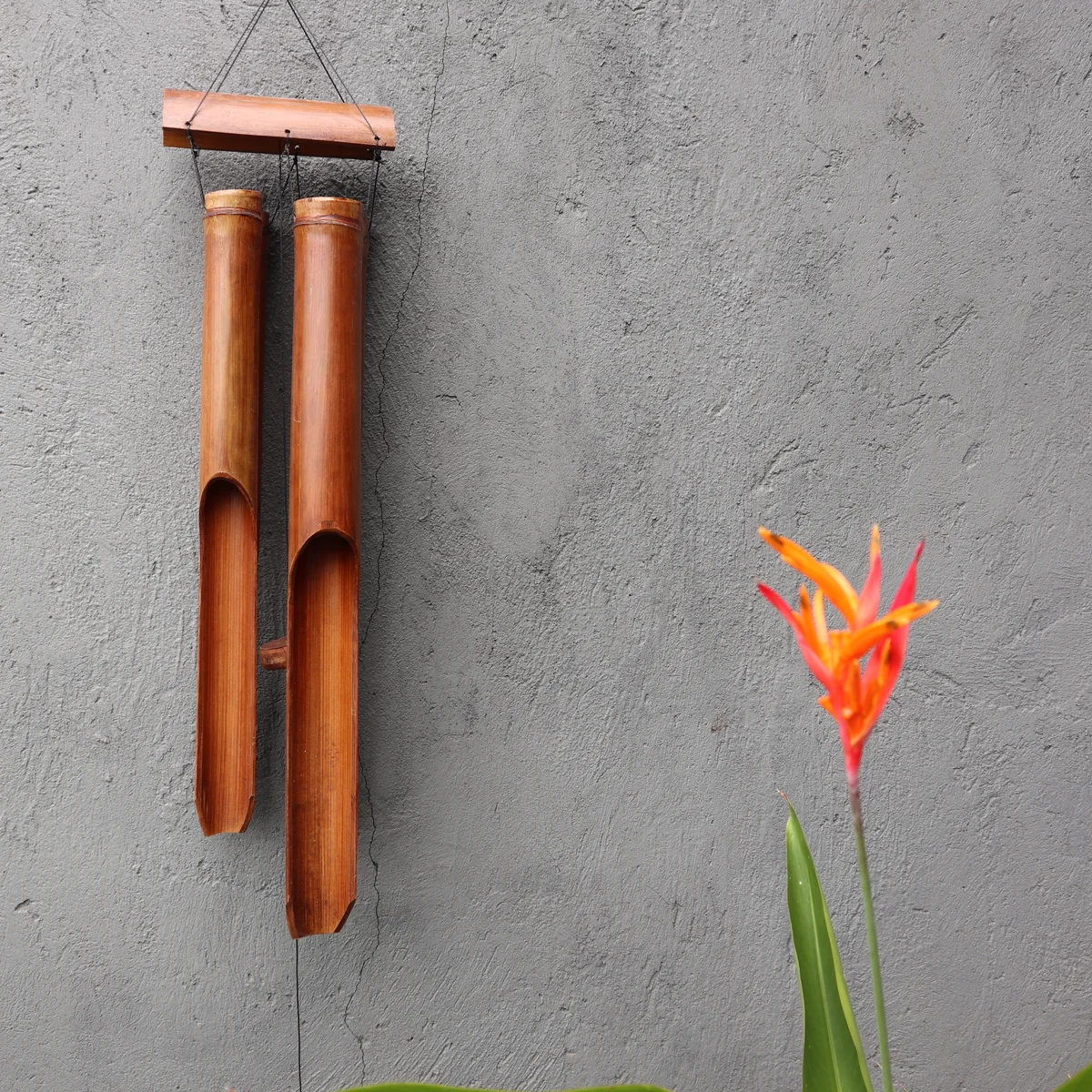 Outdoor bamboo chimes with four large natural finish tubes hanging against a plain background