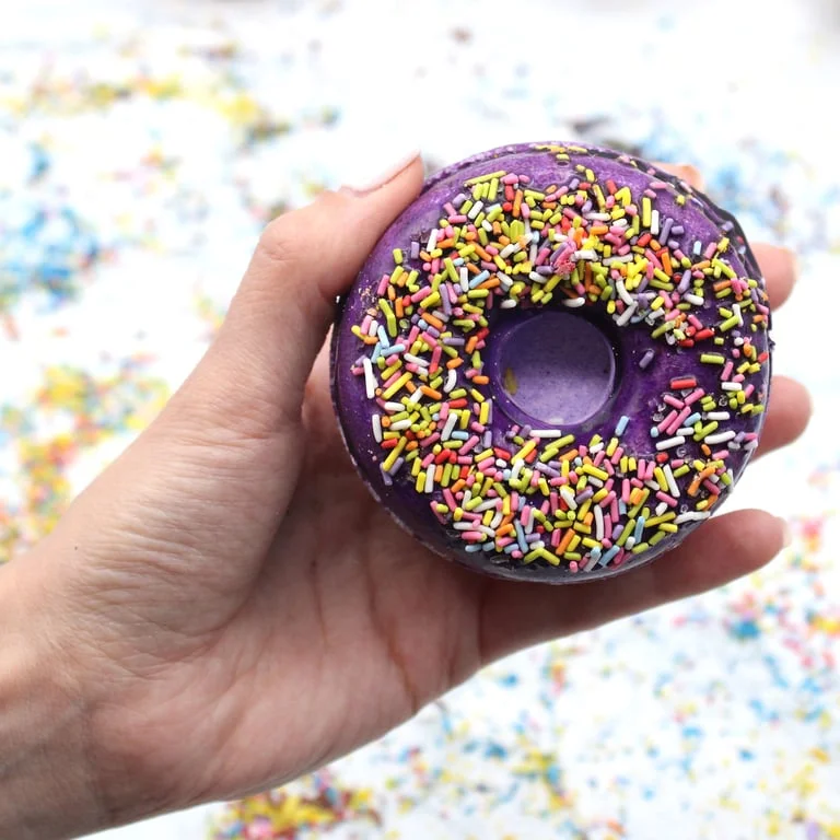 Blackberry and almond scented bath bomb shaped like a donut, pearl‑shimmering with specks, on neutral background.