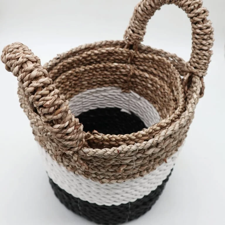Three woven seagrass baskets—dark grey, white storage basket, natural—displayed together on a neutral background