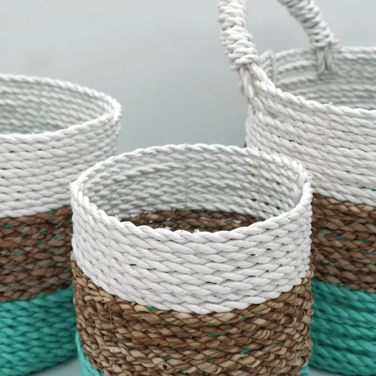 White seagrass basket beside green and natural seagrass baskets on a wooden table.