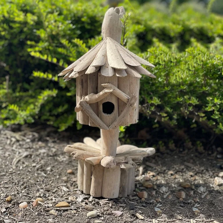 Wooden driftwood birdbox mounted on a simple stand, a garden bird feeder box in a garden backdrop
