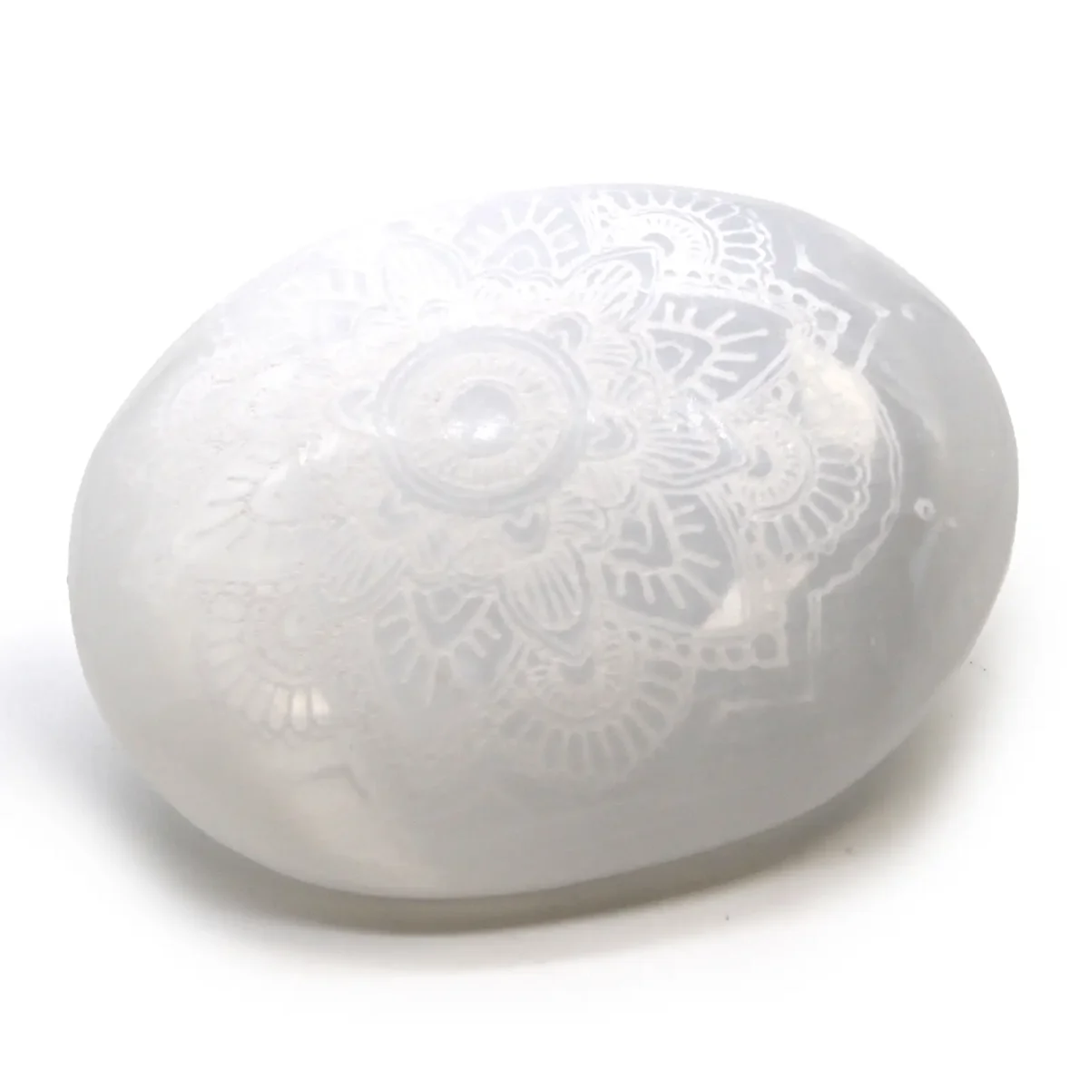 Smooth selenite palm stone with intricate mandala engraved stone design on its surface against a white background