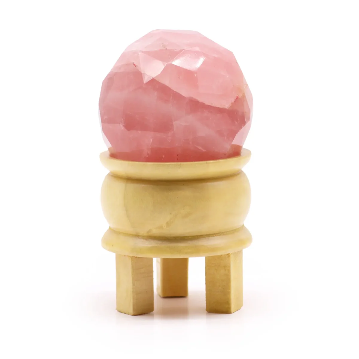 Faceted rose quartz gemstone healing ball resting on a wooden stand against a white background
