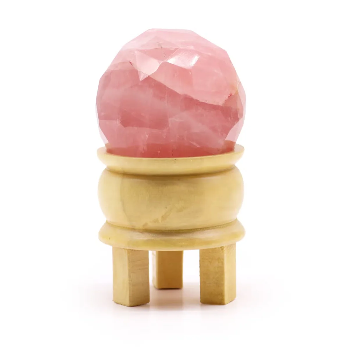 Faceted healing ball made of rose quartz on a wooden stand with a soft white background