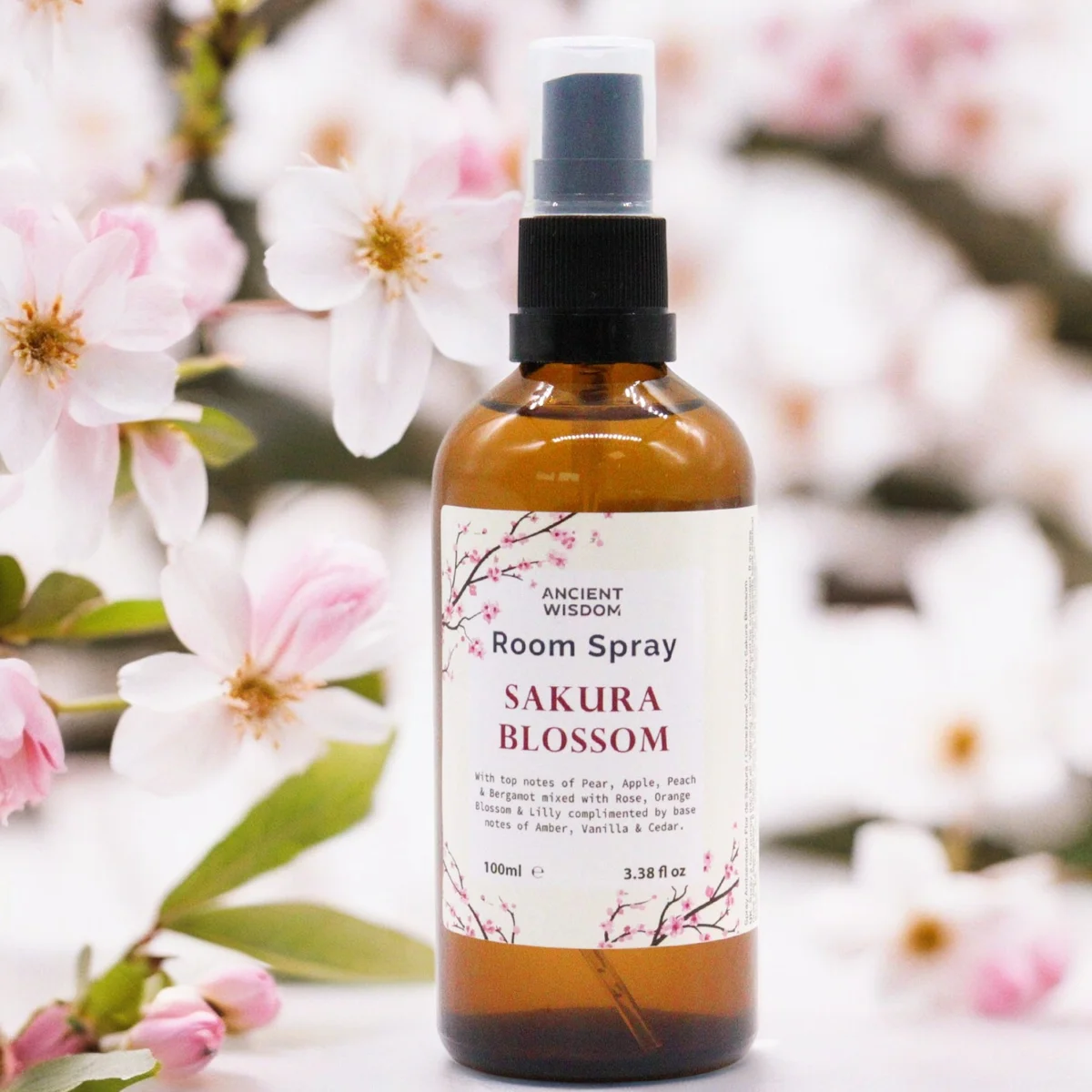 White glass spray bottle labeled “Home Fresh sakura essence spray 100ml”, silver pump, subtle pink backdrop.