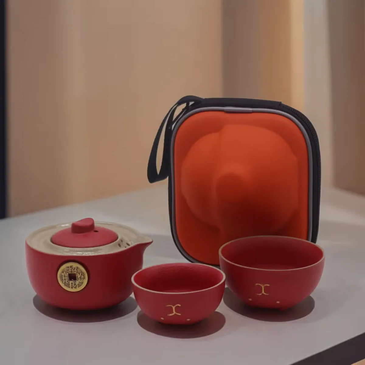 Red teapot set with two cups, featuring a playful money cat design, displayed in a compact travel pack