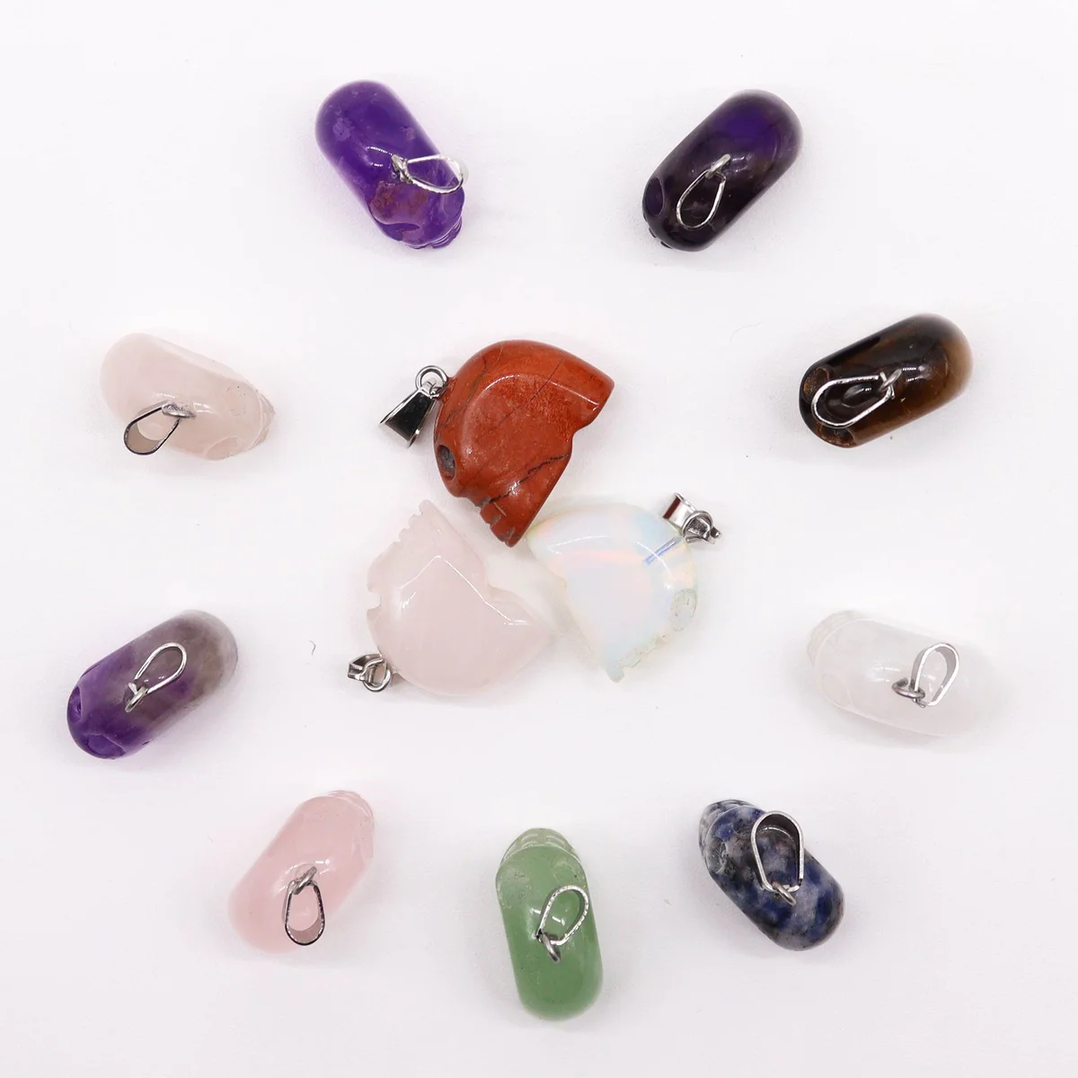 Assorted gemstone pendants: a set of 12 mini skull shapes in varied stones, showcasing vibrant colors on a simple background.