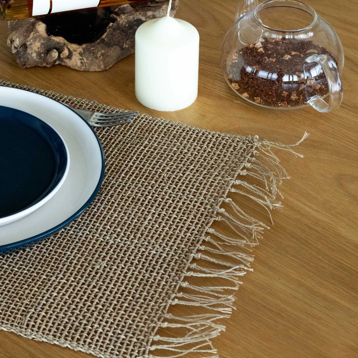 Natural seagrass placemat with fringe detailing laid flat on a white background