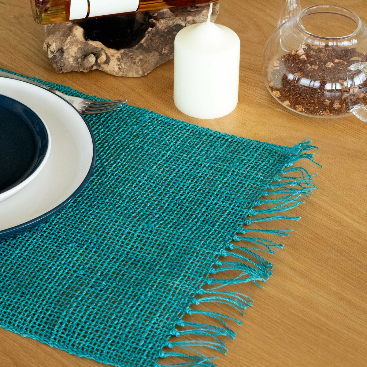 Turquoise seagrass table mat with natural fringe detailing on a white background, shown flat and round