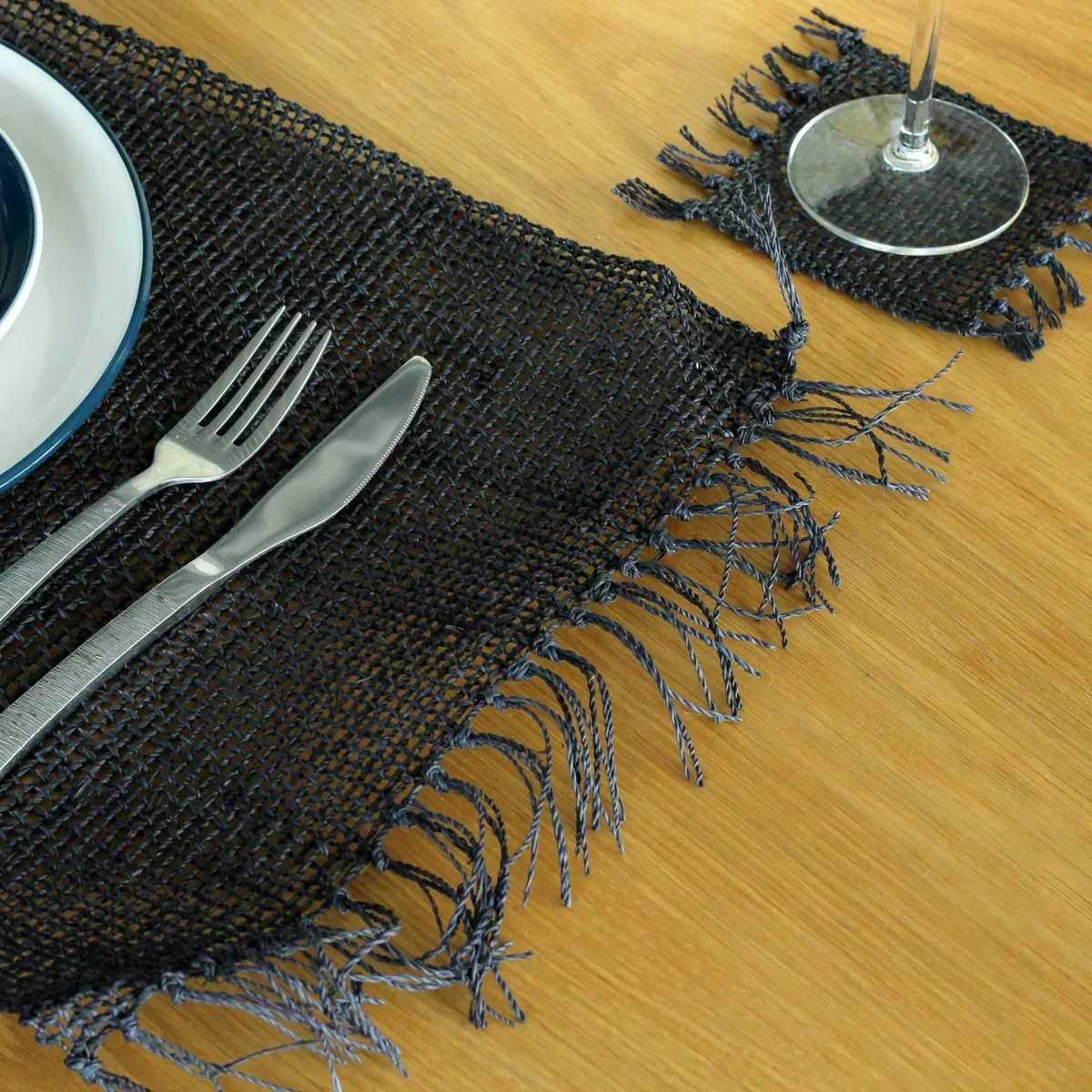Black natural seagrass placemat with fringe detailing, round shape, flat woven texture on white background