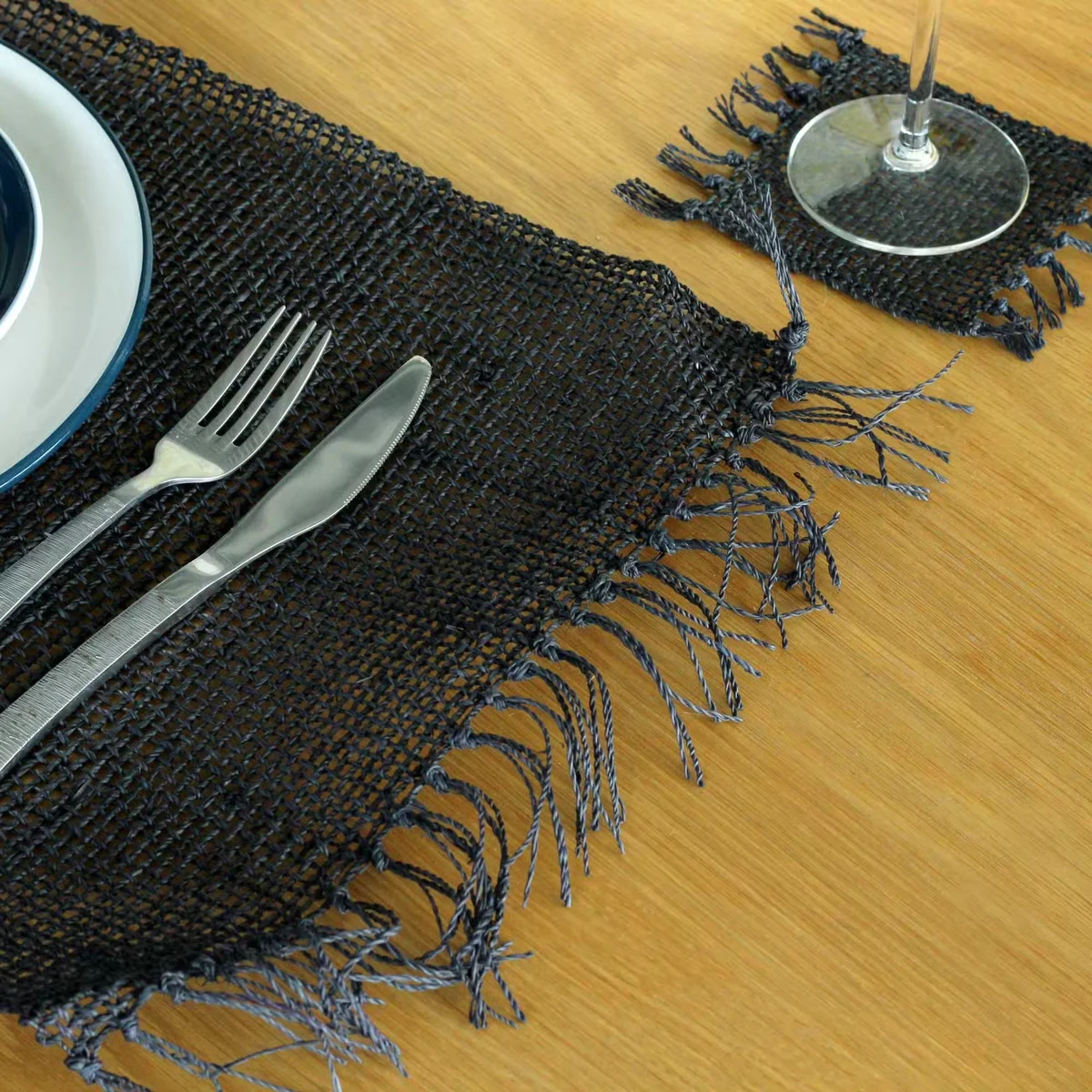 Black seagrass fringe eco friendly placemat with natural woven texture, laid flat on a white surface