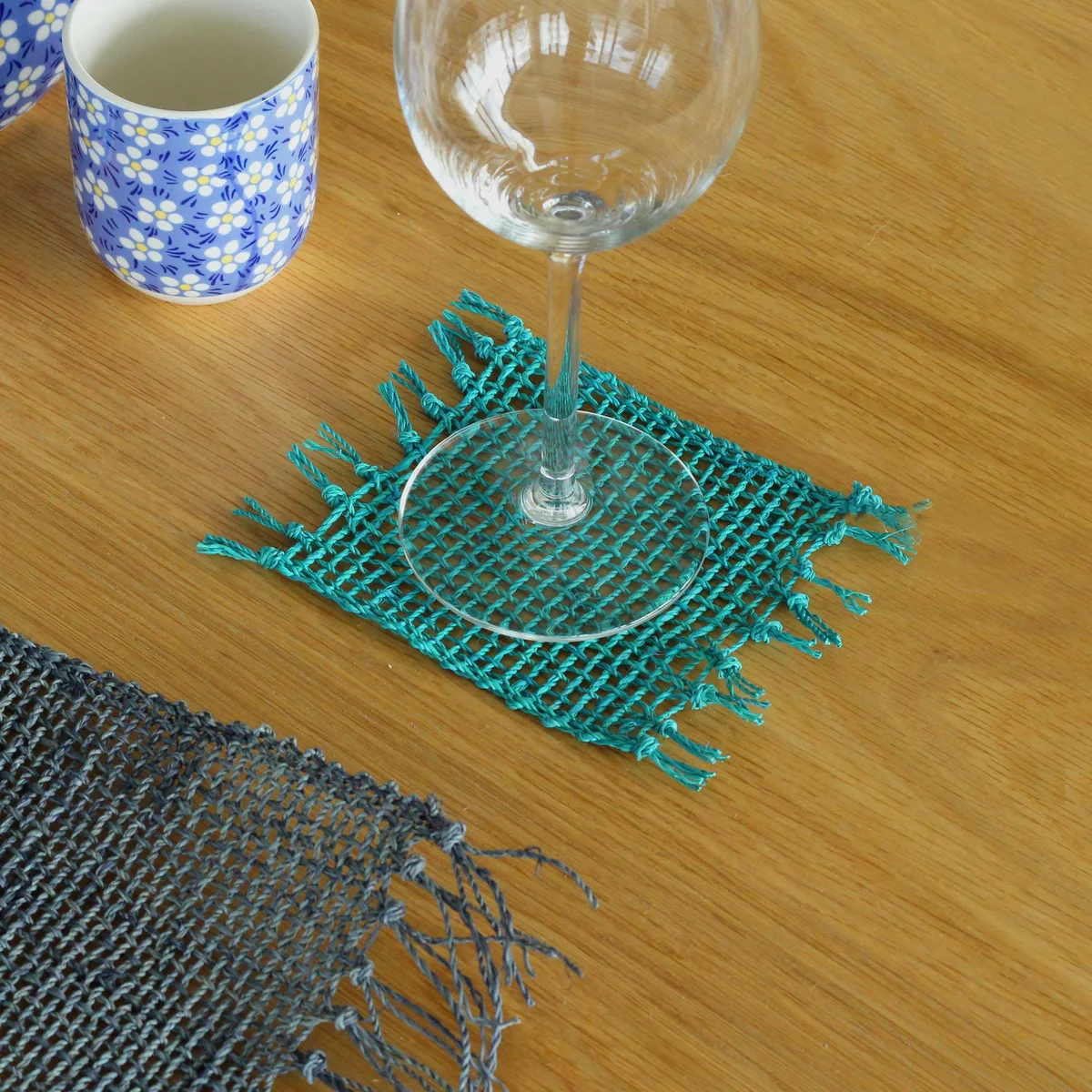 Set of 4 natural seagrass fringe edge coasters in turquoise, stacked with visible textured edges on white background