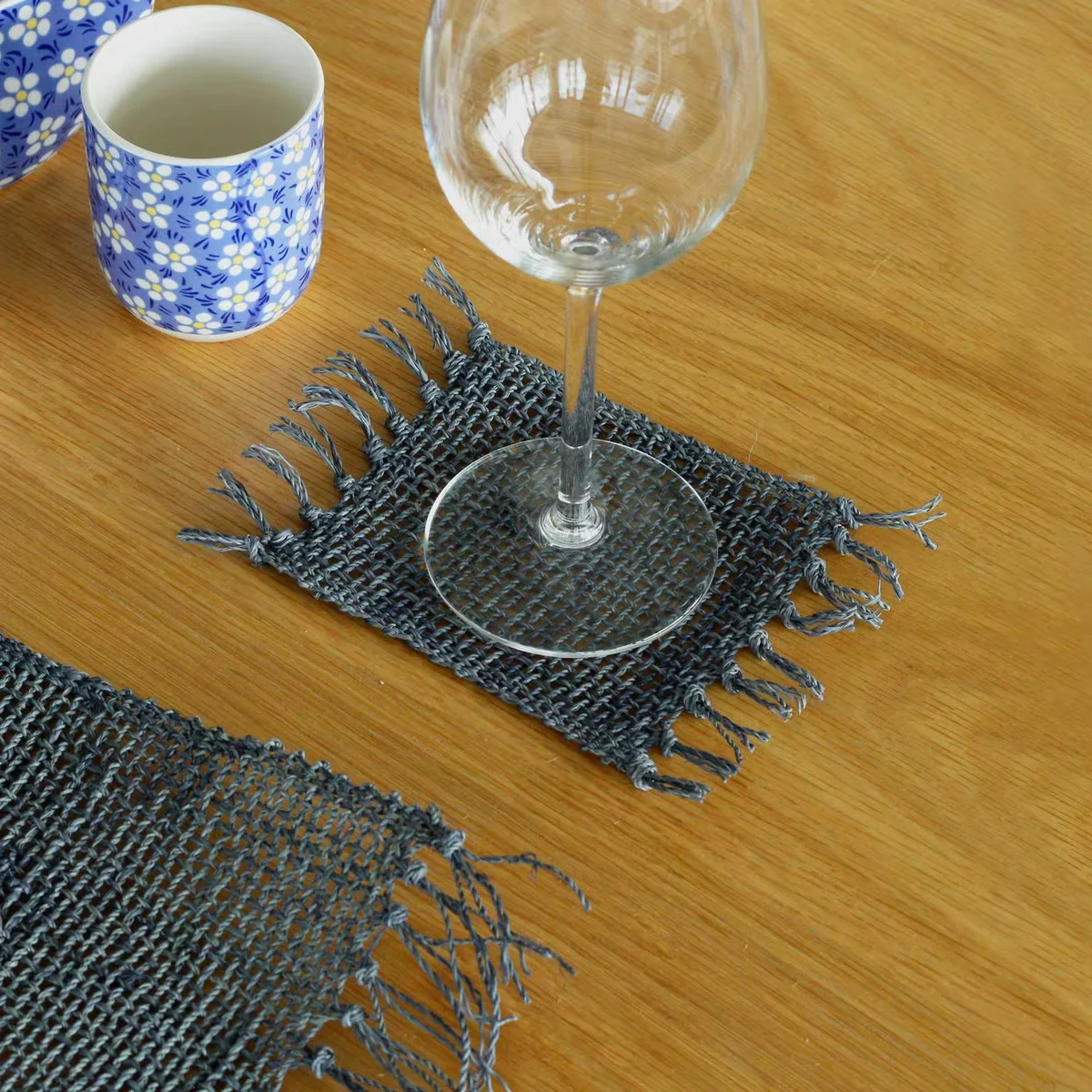 Set of four charcoal coaster set made from natural seagrass with fringe detailing, stacked on a white surface