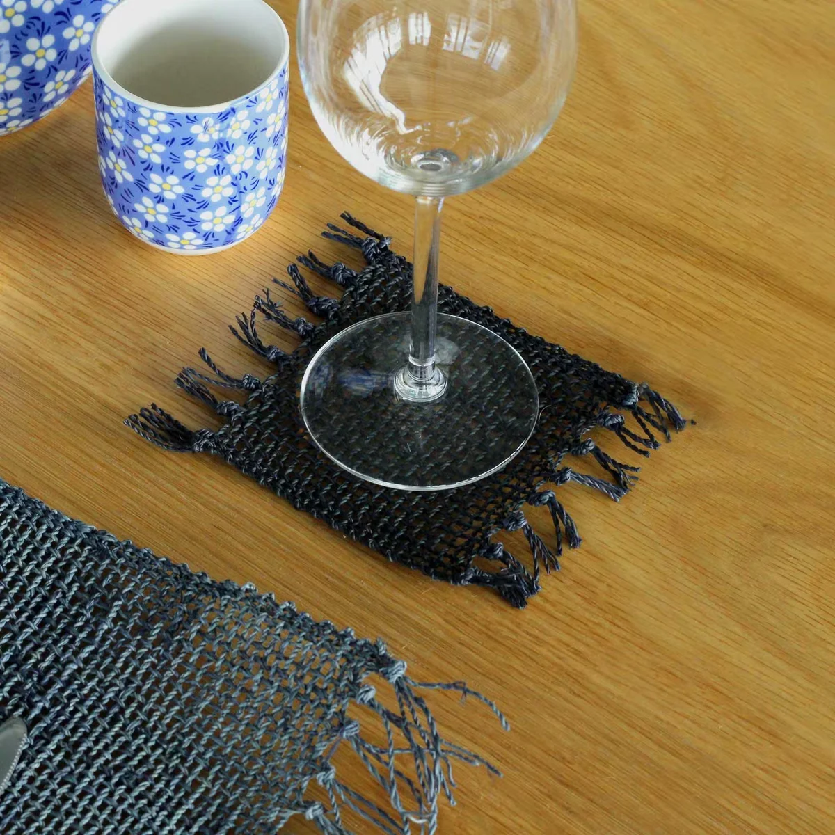 Set of 4 black seagrass coasters with natural fringe edges stacked on a white surface