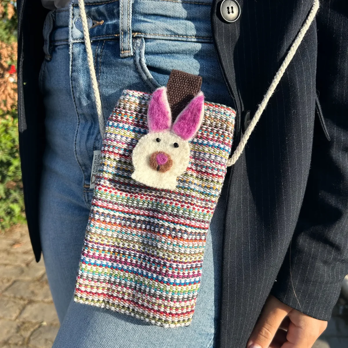 Pink phone holder bag with stripes and bunny decor on front, designed to hold a phone securely