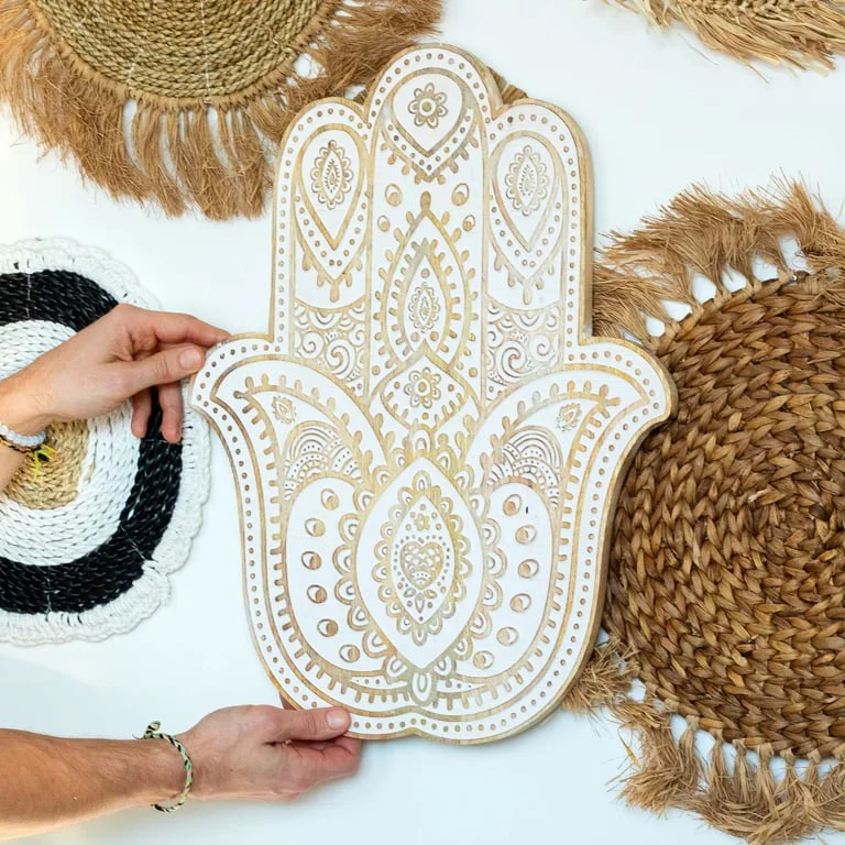 Whitewashed mango wood wall plaque featuring a carved Hamsa hand graphic.