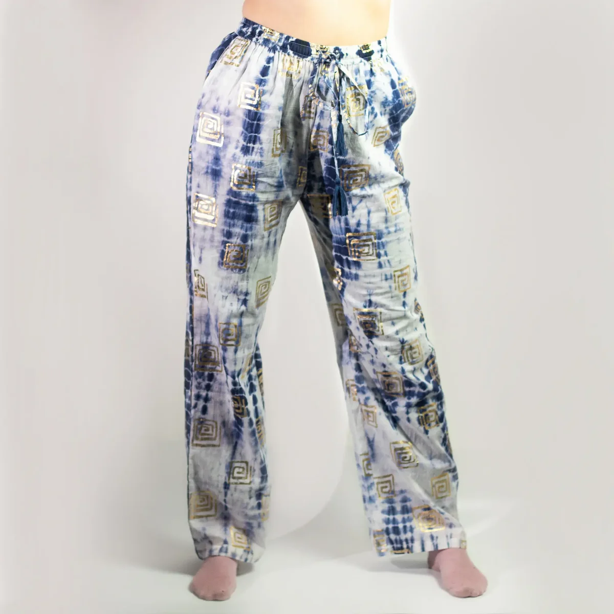 Nomad sari lounge pants in blue tie‑dye, featuring a gold Greek motif, shown folded on a flat surface.