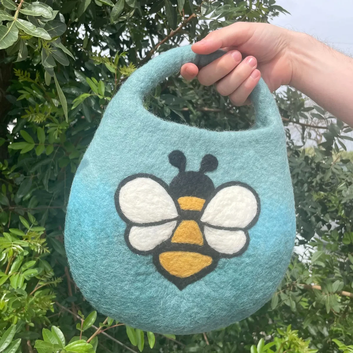 Blue green handbag with a single handle and magnet closure, water felted bee bag design.