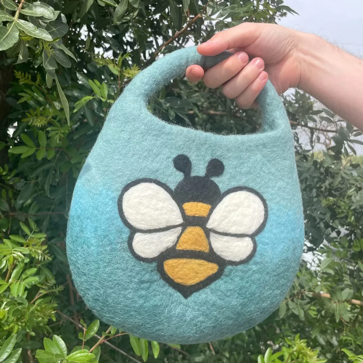 Blue‑green water‑felted bee bag with a single handle, featuring a built‑in magnet.
