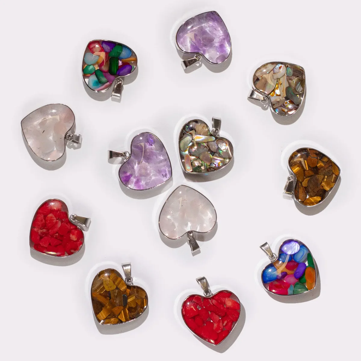 Assorted gemstone pendants in steel cases, featuring heart shapes with colorful chips and shells.