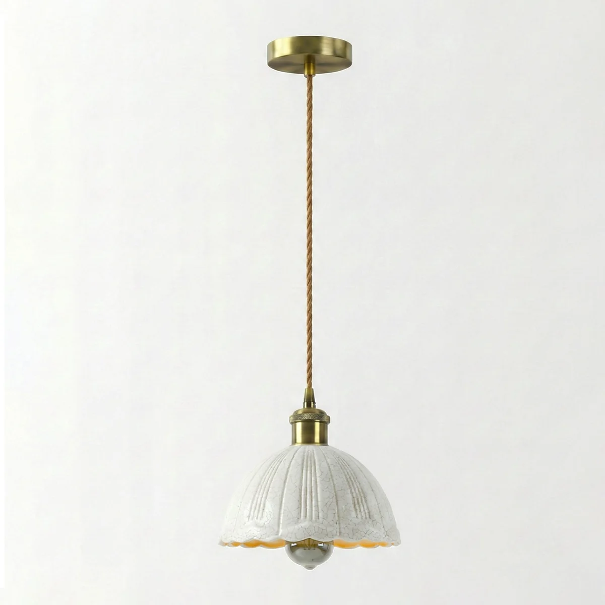 White crackle glass pendant light with scalloped edges, brass hardware, and adjustable fabric cord hanging from ceiling